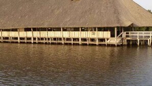 Une grande construction à toit de chaume qui s’étend au-dessus de l’eau, probablement un abri pour bateaux ou un entrepôt.