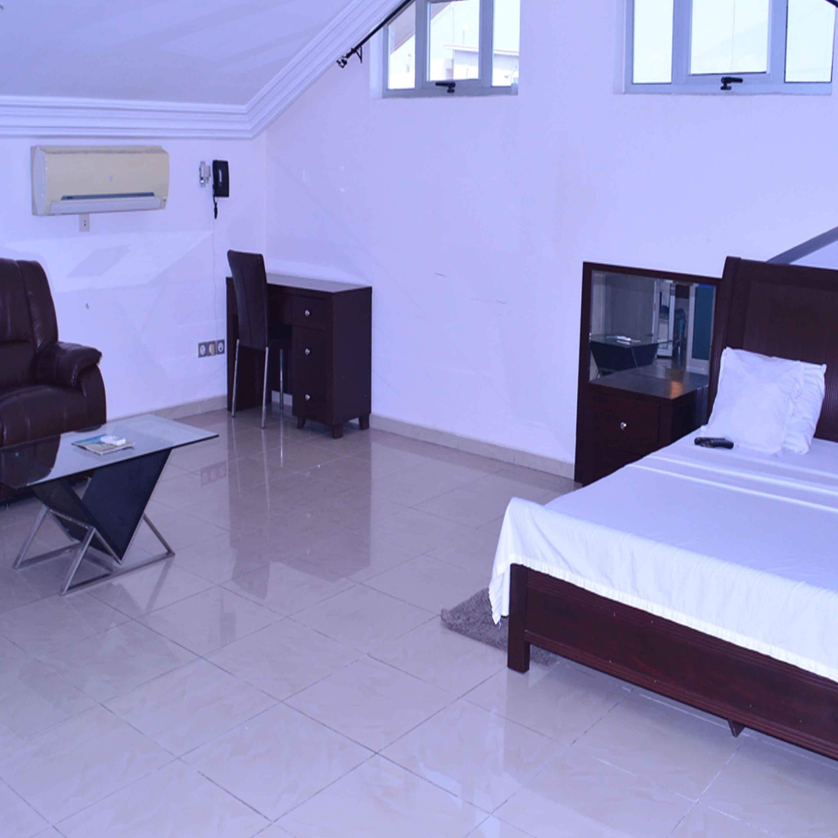 A bedroom with a bed, a desk, a chair, and a sofa.
