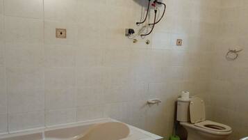 Un baño con bañera, inodoro y calentador de agua montado en la pared.