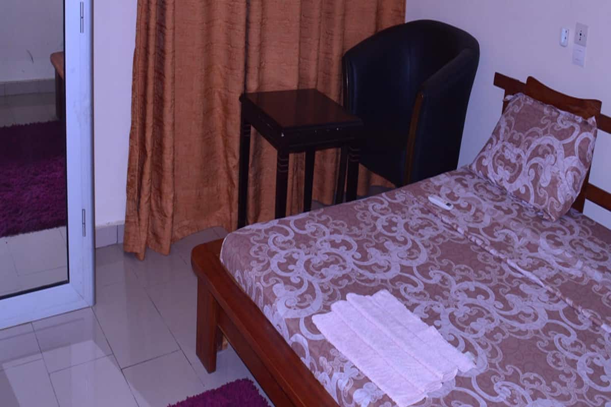 Un dormitorio con cama, una silla, una mesita, un espejo y una cortina.