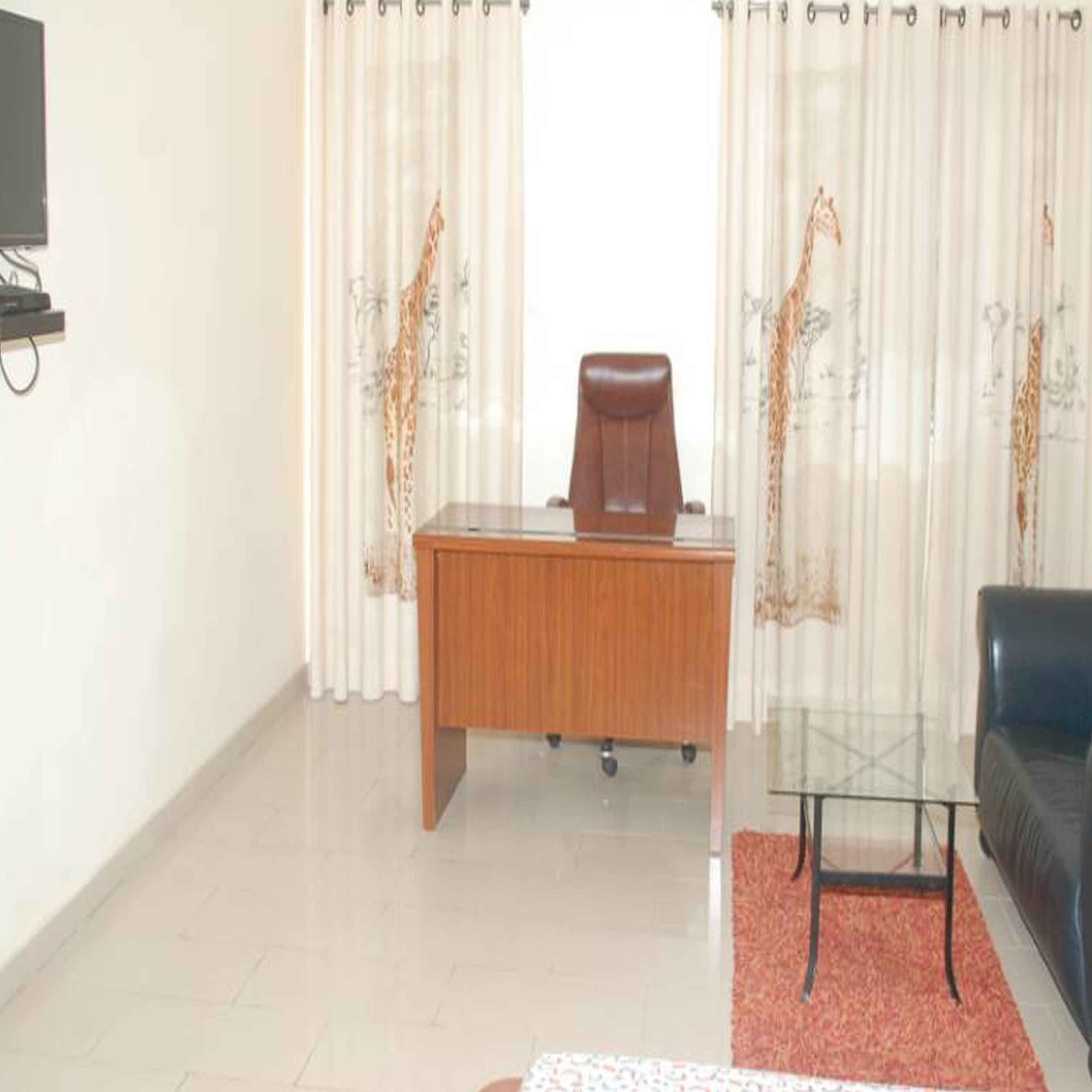 A room with a wooden desk, a black leather sofa, and a glass coffee table.