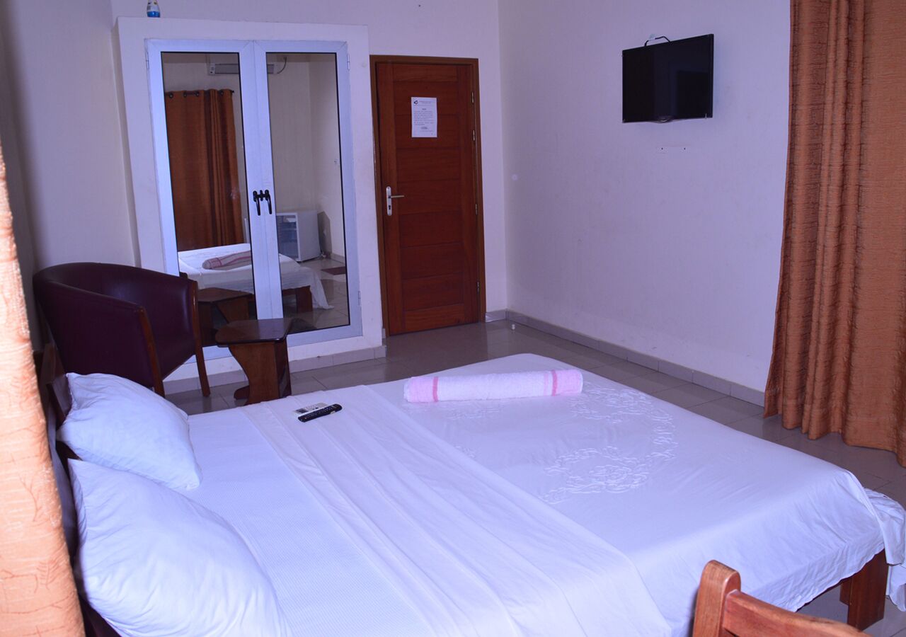 Une chambre d’hôtel avec un lit, une chaise, un bureau, une porte et une petite fenêtre.