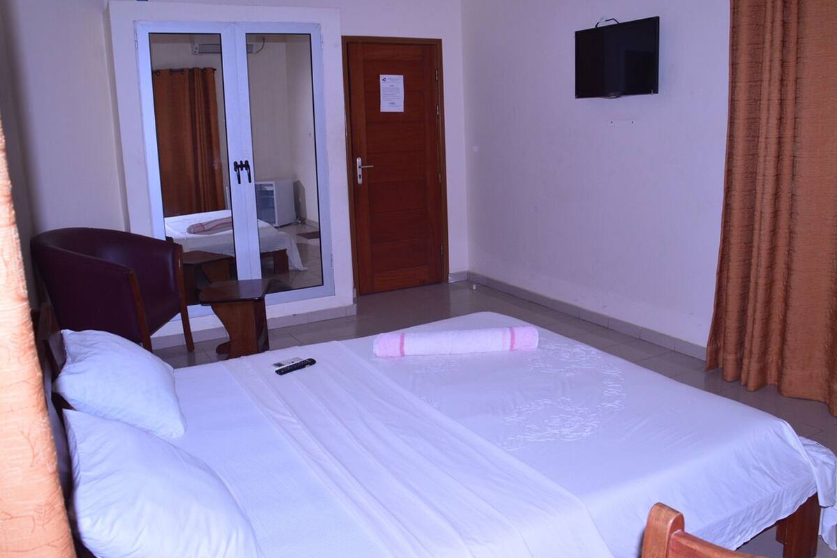 Habitación de hotel con cama, una silla, un escritorio, una puerta y un ventanal pequeño.
