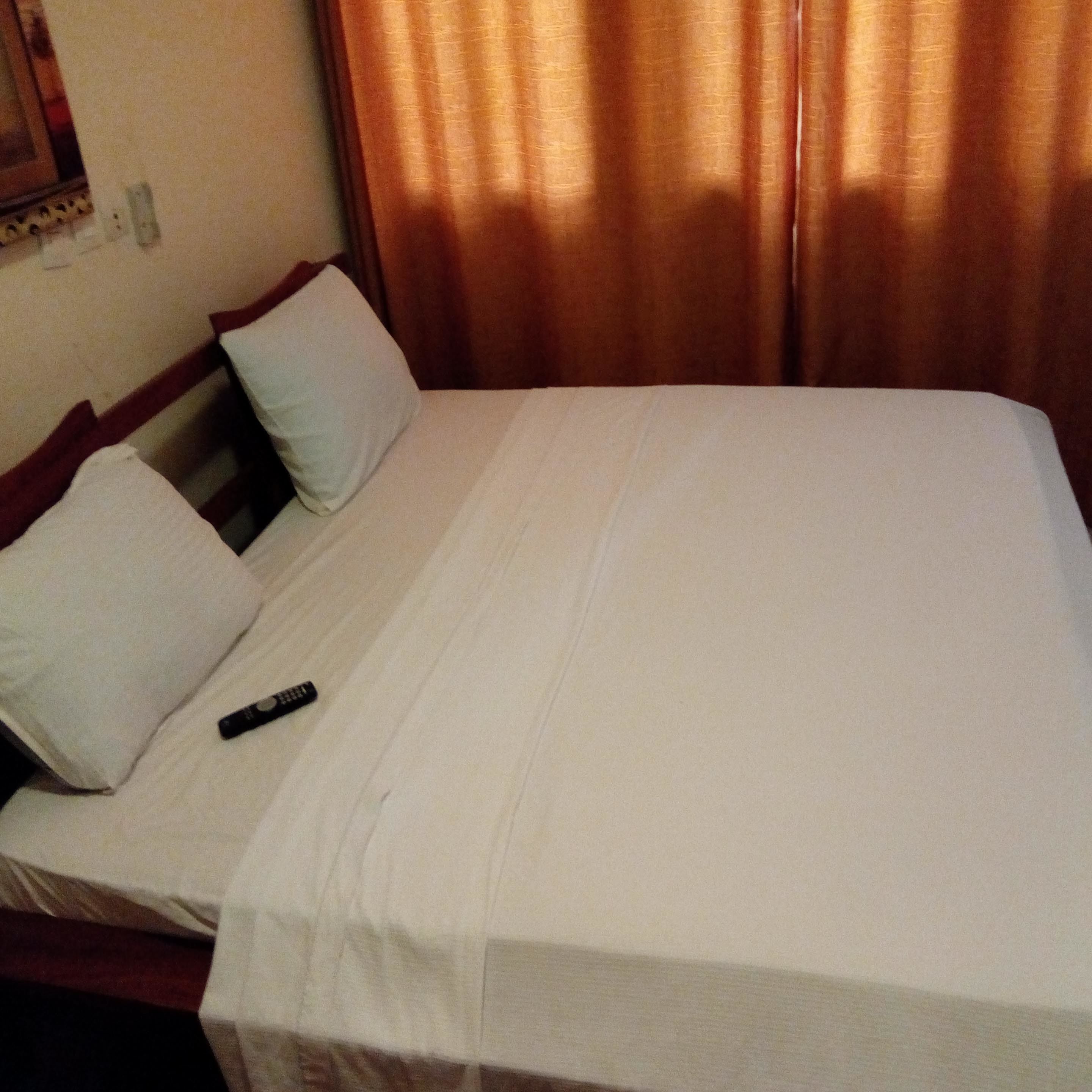 A hotel room with a bed, pillows, and a remote control on the bed.