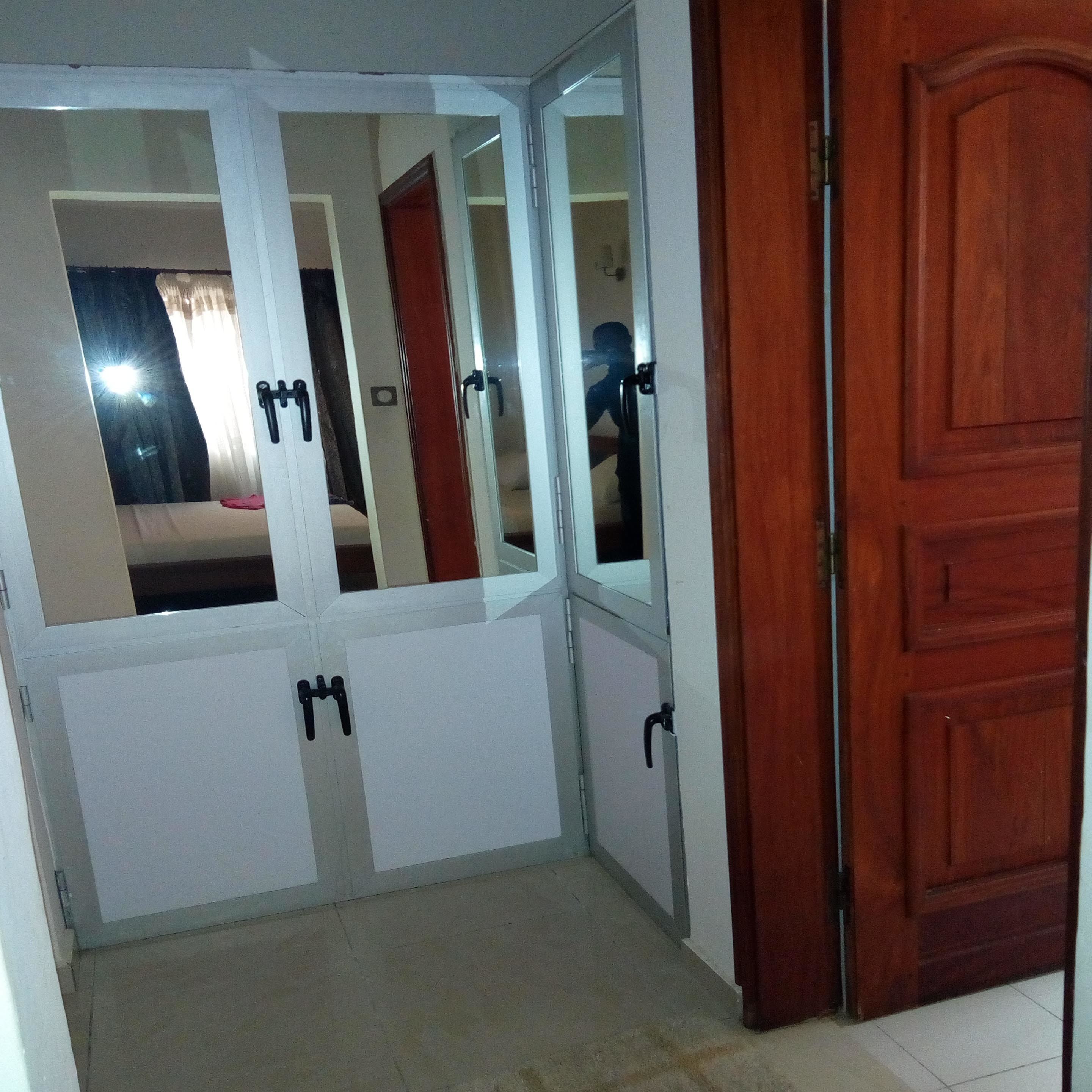 Une pièce avec une porte en bois, un mur blanc et un miroir dans lequel se reflète une personne.