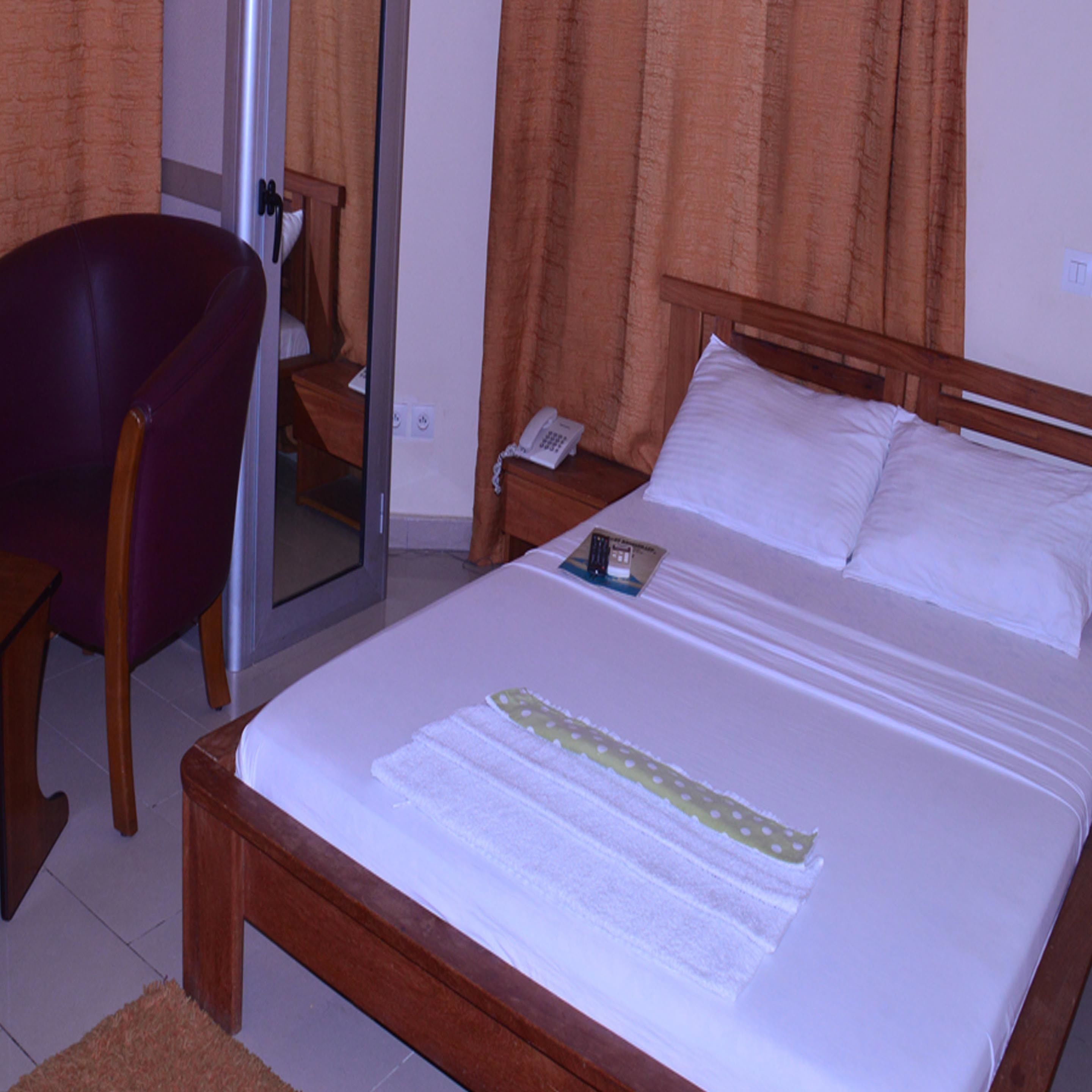 Une chambre d’hôtel avec un lit, une chaise, une table de chevet et un miroir.