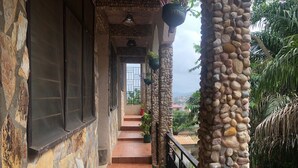 A stone-walled building with a balcony, potted plants, and a view of the surrounding landscape. - Legassi Gardens Apartments (Kwabenya)