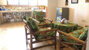 A kitchen with a stone backsplash, wooden chairs with patterned cushions, a refrigerator, and a window with curtains. - Legassi Gardens Apartments (Kwabenya)