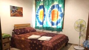 A bedroom with a bed, pillows, a green rug, a wall-mounted fan, and a painting. - Legassi Gardens Apartments (Kwabenya)
