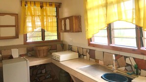 A kitchen with a stove, sink, and windows with yellow curtains. - Legassi Gardens Apartments (Kwabenya)