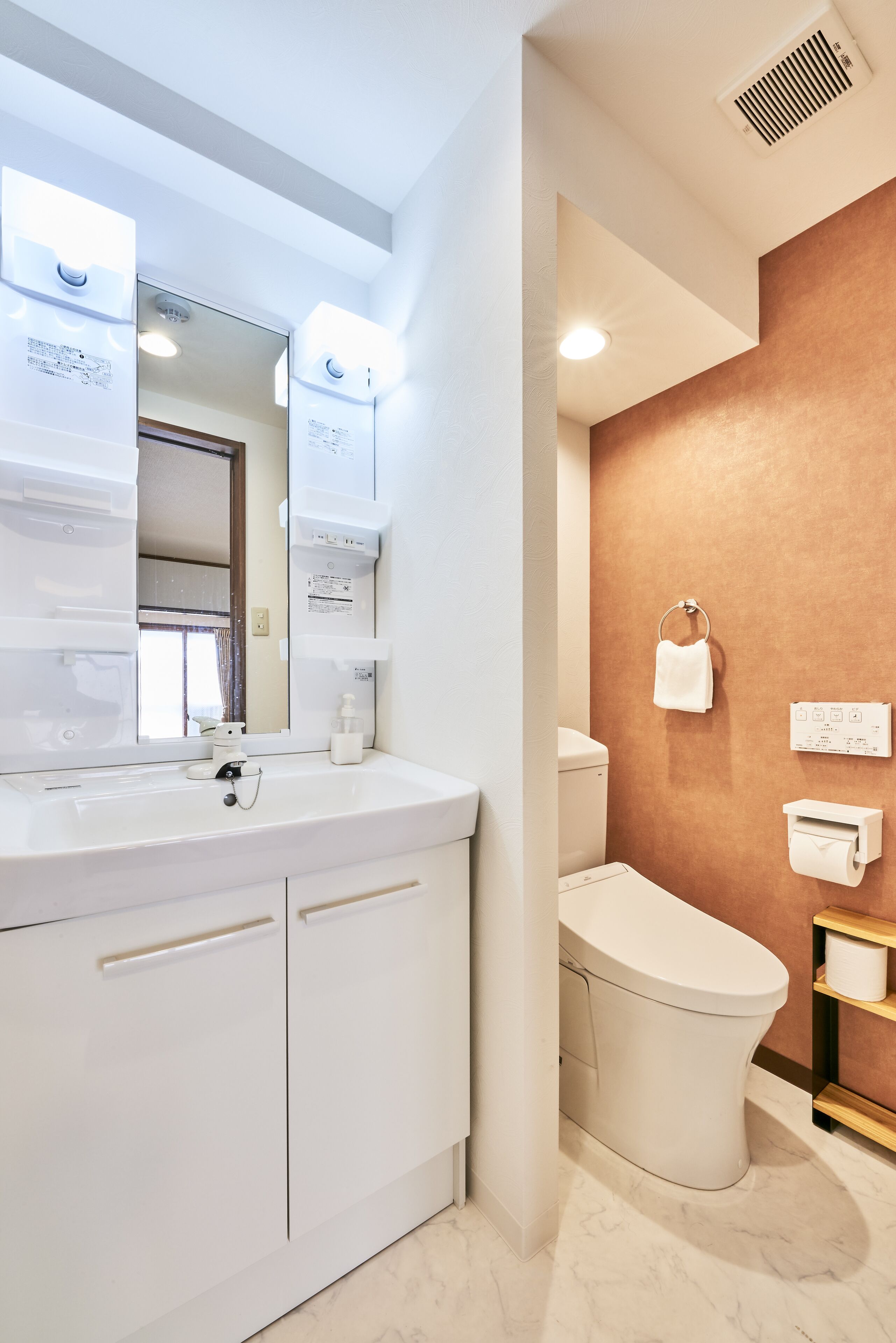 A modern bathroom with a white vanity, a large mirror, a toilet, and a towel rack.