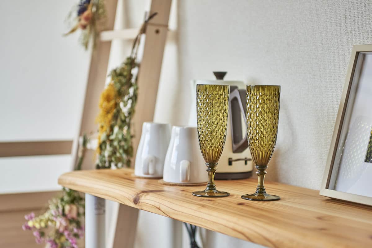 Une étagère en bois sur laquelle reposent deux verres de couleur or, une bouilloire blanche et un tableau encadré.