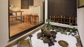 Un intérieur moderne comprenant un coin repas, un petit jardin agrémenté de rochers et de plantes, et une porte coulissante donnant sur une autre pièce.