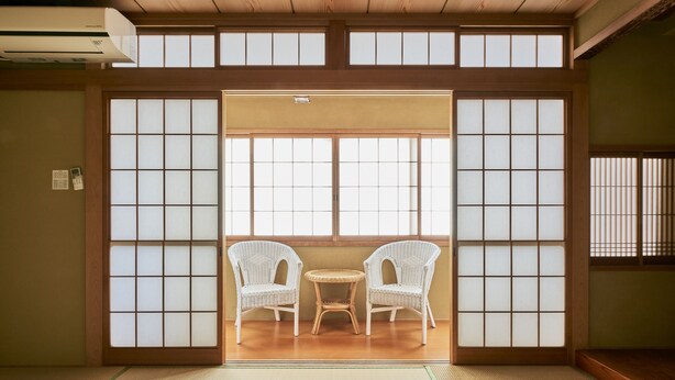 Une pièce de style japonais traditionnel, avec un sol recouvert de tatamis, une porte coulissante en papier de riz (shoji) et deux chaises en osier blanc disposées autour d’une petite table.