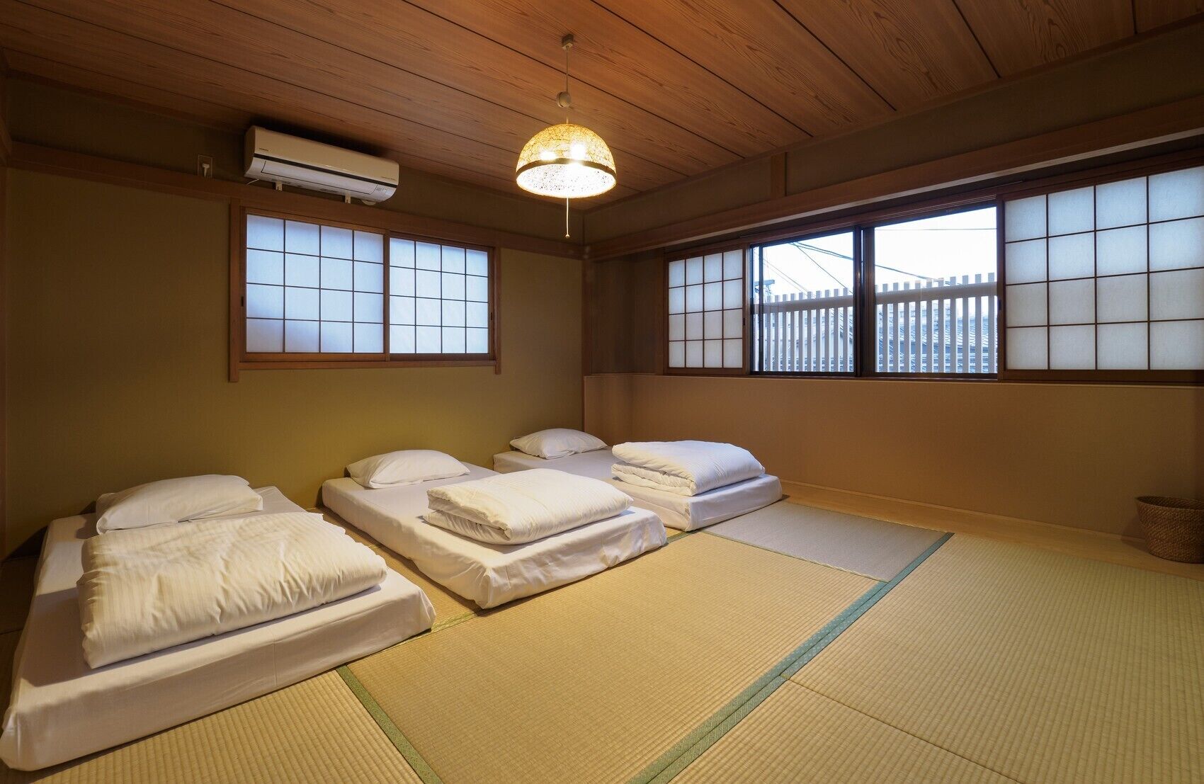 A traditional Japanese room with tatami flooring, a futon bed, shoji screens, and a hanging light fixture.