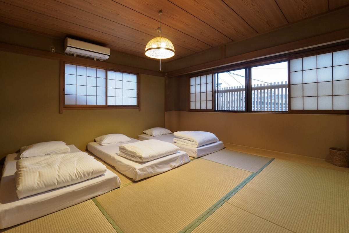 Une pièce de style japonais traditionnel, avec un sol recouvert de tatamis, un futon servant de lit, des paravents shoji et un luminaire suspendu.