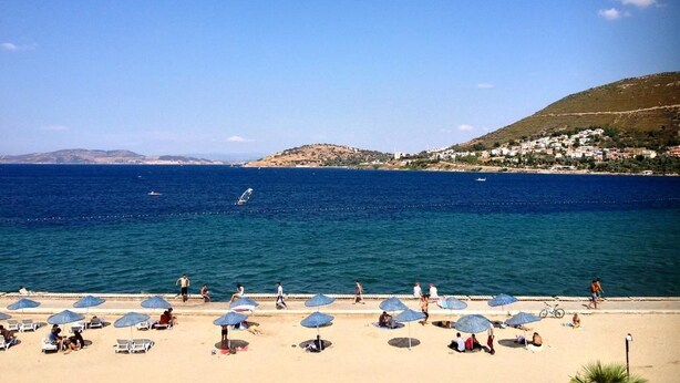 A beach with umbrellas and people. - Nemrut Bay Otel (Foça)
