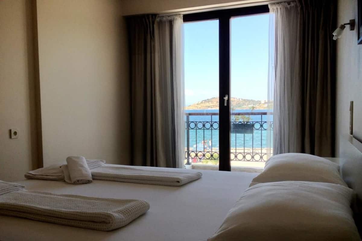 A hotel room with a bed, towels, and a view of a balcony with a railing and a distant landscape.