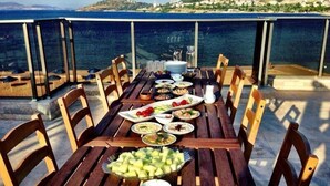 A wooden table set with various dishes and a glass of water, overlooking a coastal landscape. - Nemrut Bay Otel (Foça)