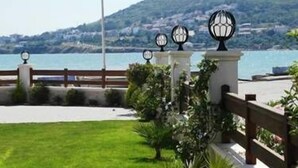 A coastal promenade with a grassy lawn, a wooden fence, and decorative lamp posts. - Nemrut Bay Otel (Foça)