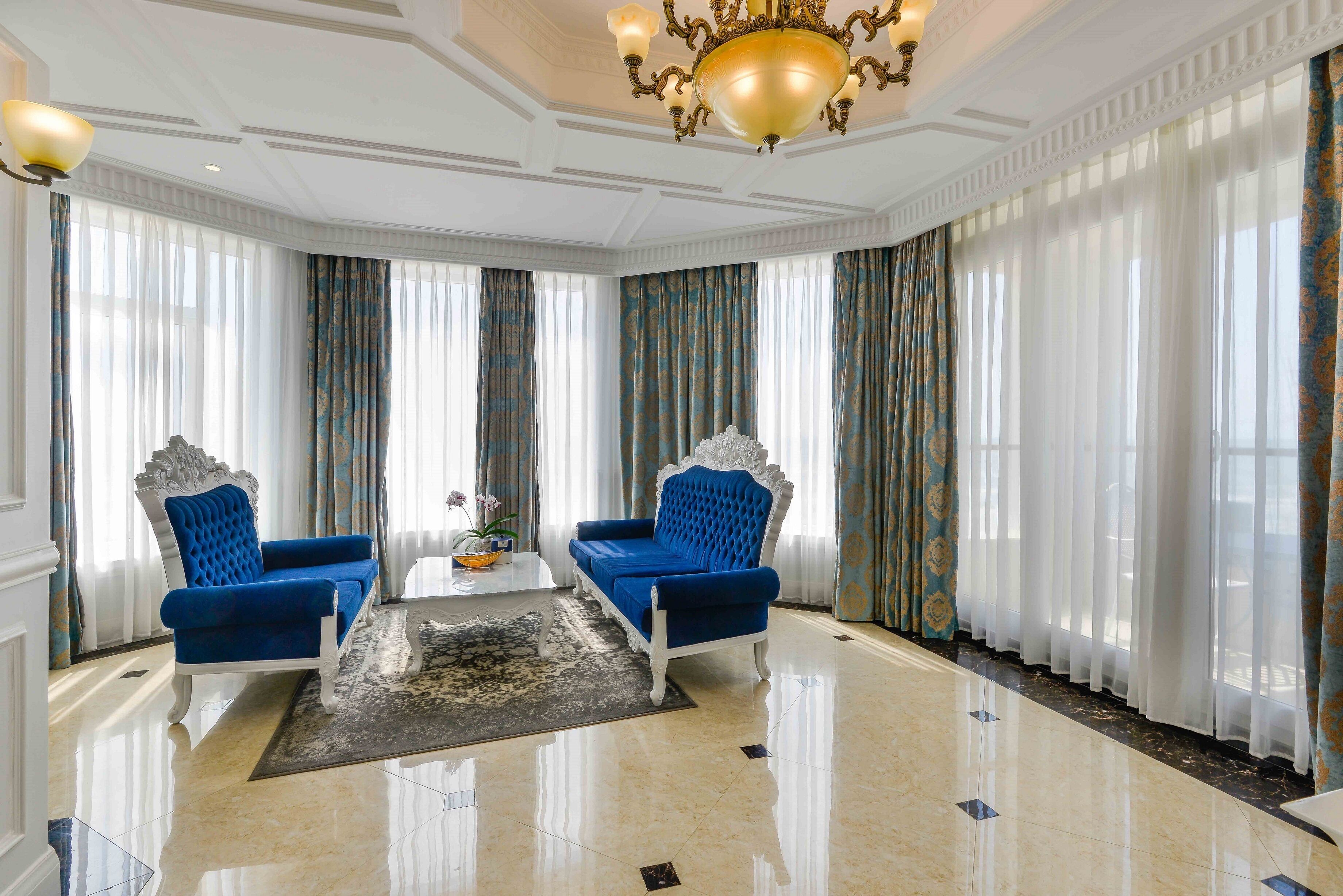 A spacious room with two blue armchairs, a chandelier, and large windows with curtains.