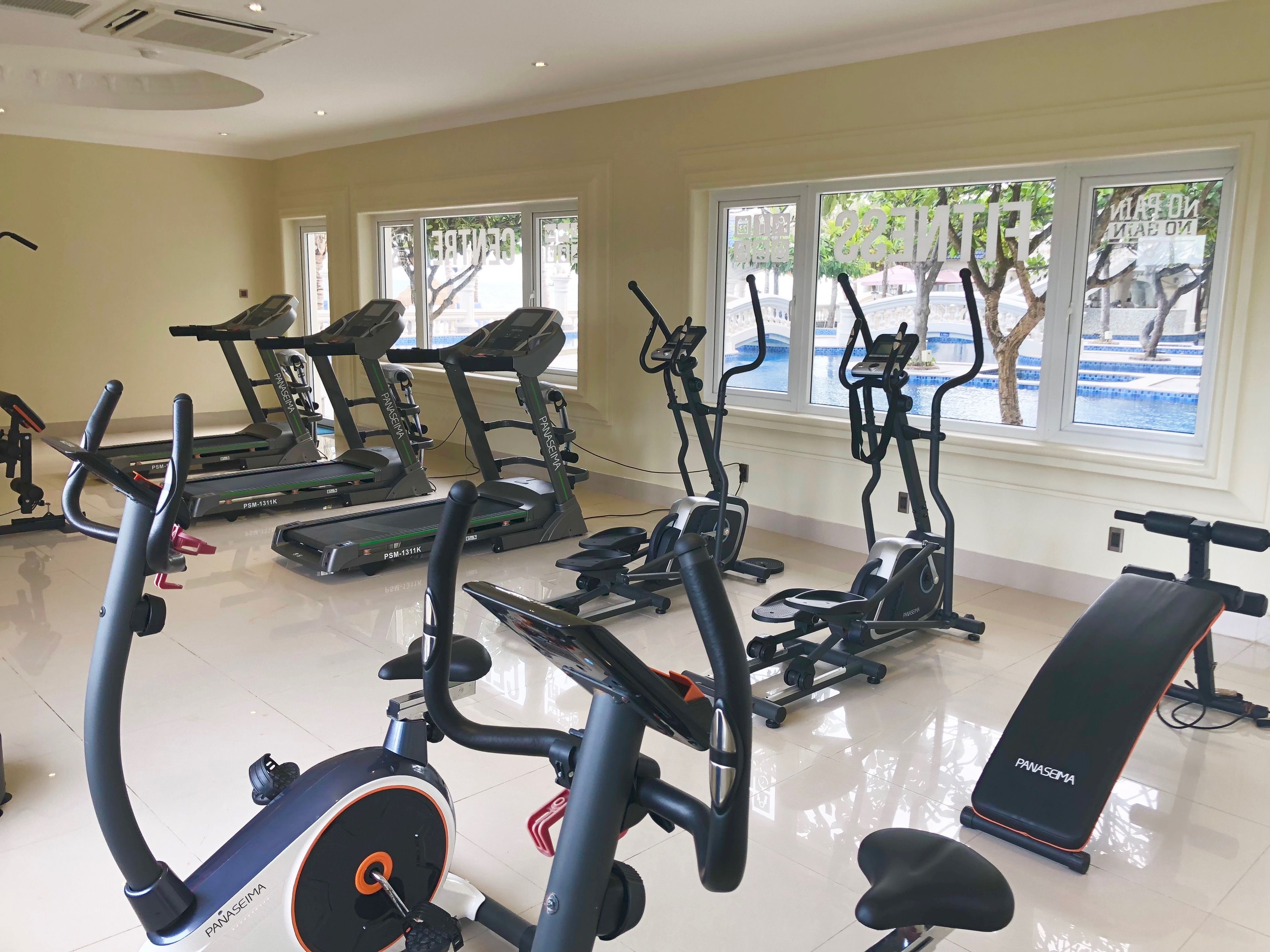 Ein Fitnessstudio mit Laufbändern, Crosstrainern und einer Bank.