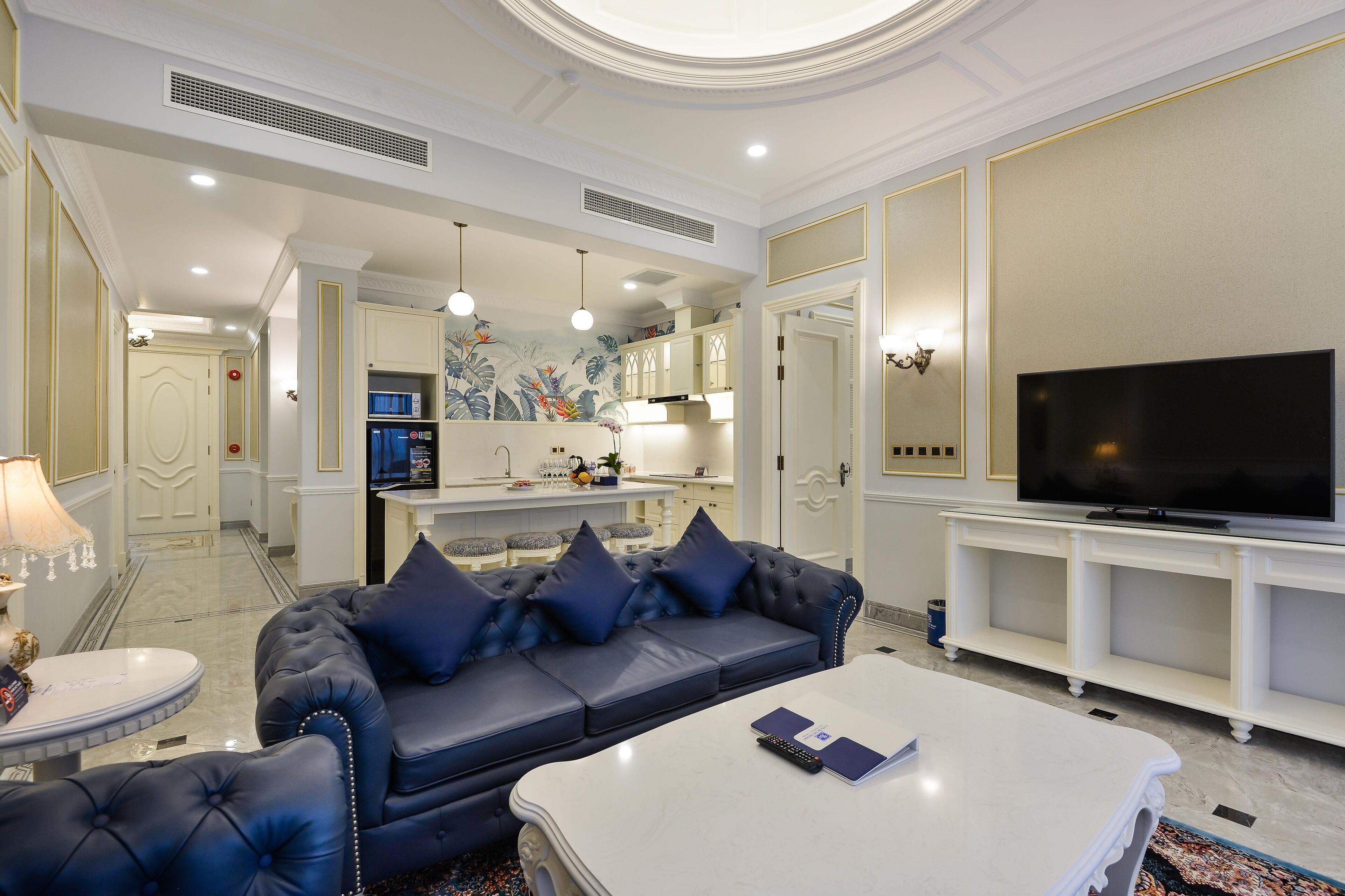 A modern living room with a blue sofa, a white coffee table, and a flat-screen TV on a white stand.