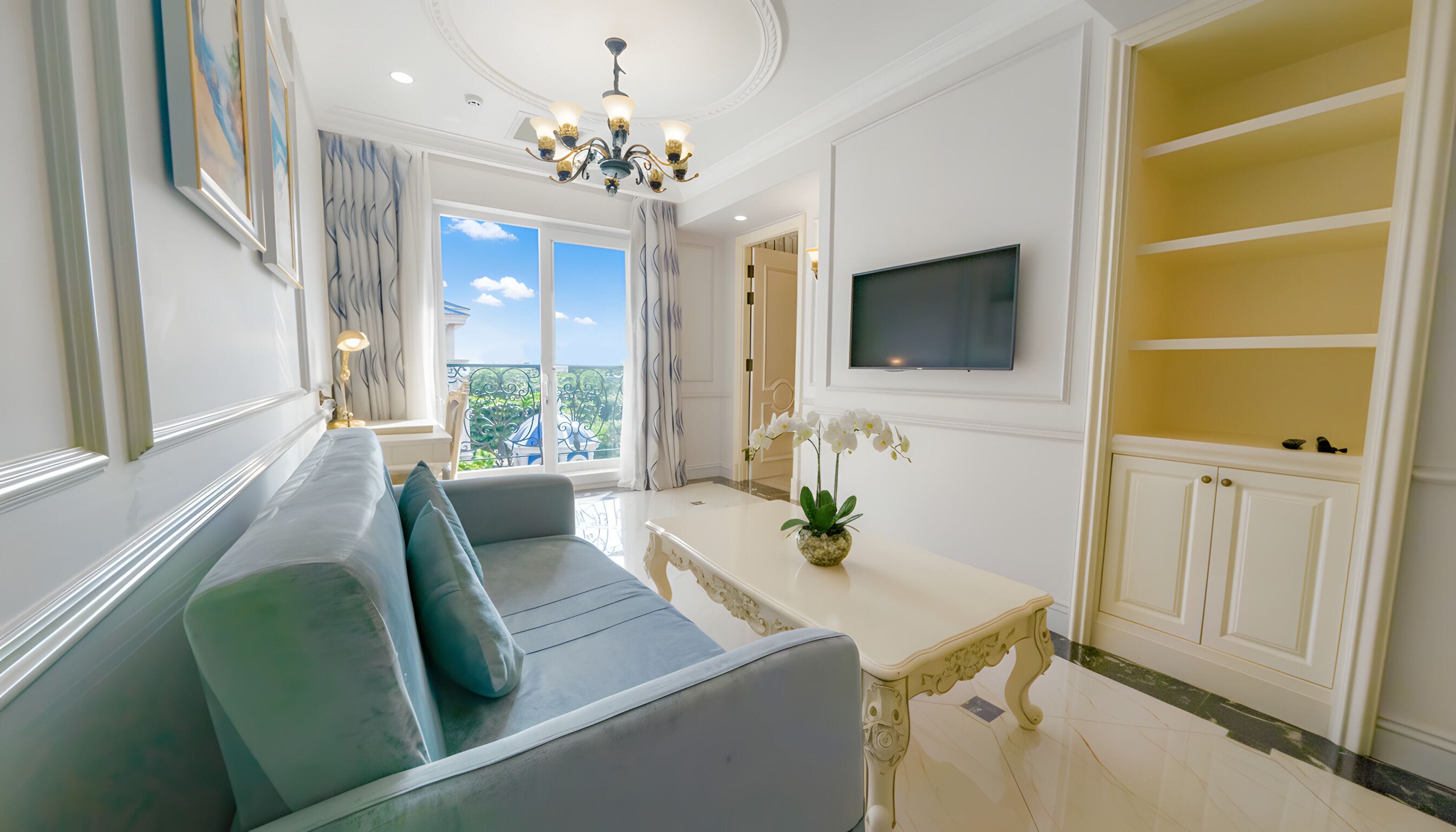 A modern living room with a sofa, a TV mounted on the wall, and a balcony with a view.