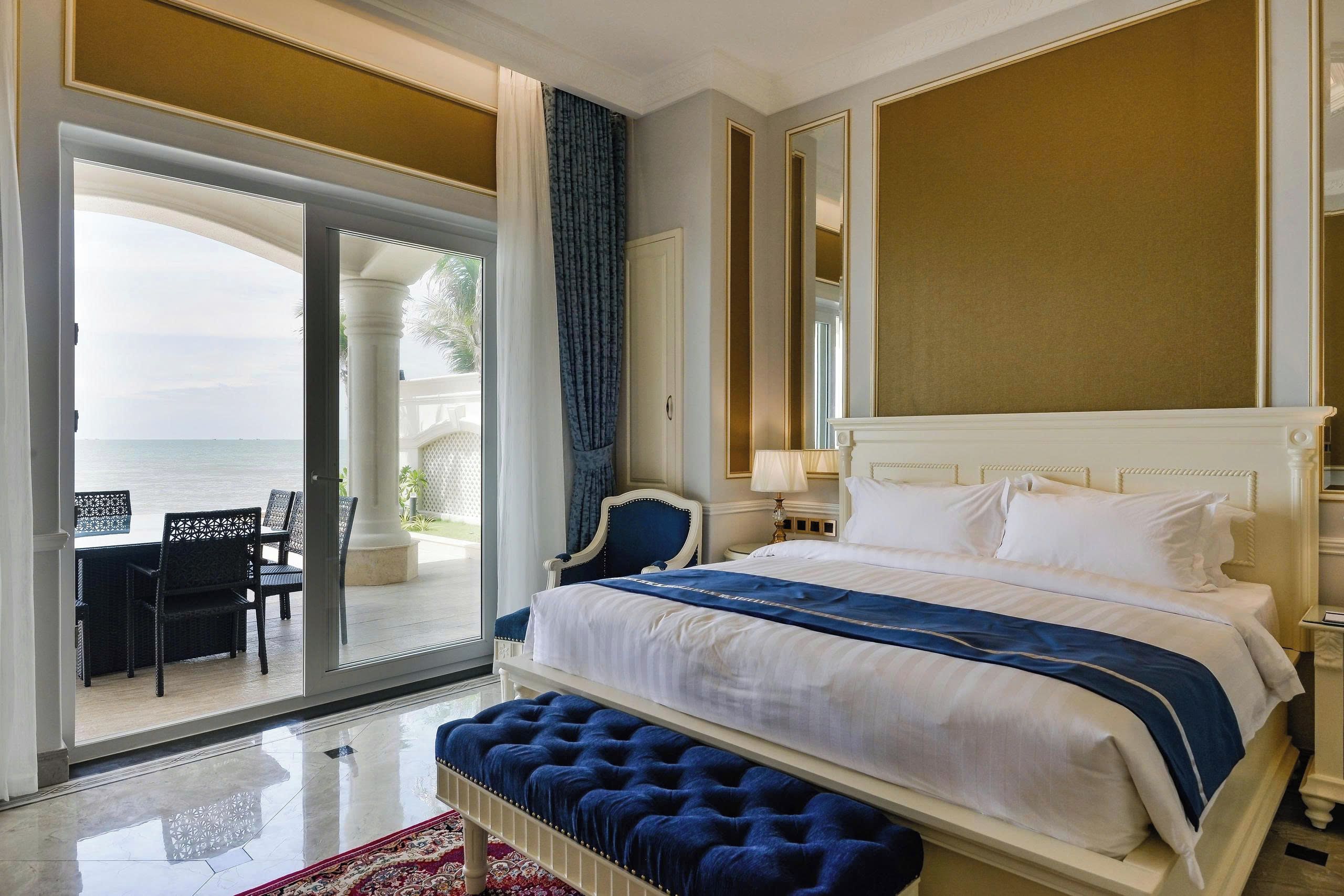 A hotel room with a large bed, a sitting area with a view of the sea, and a balcony.