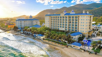 Un hotel frente a la playa con varias edificaciones, una piscina y una zona de playa.