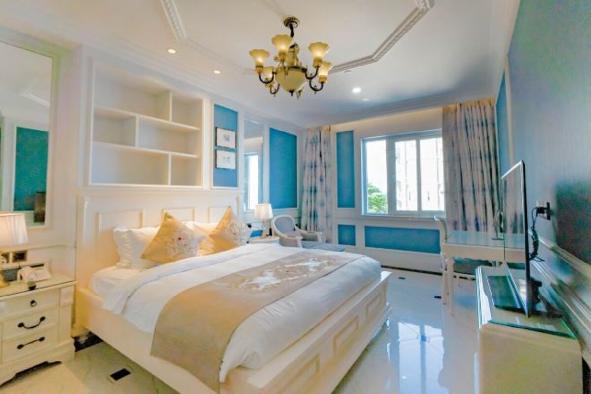 A bedroom with a large bed, bedside tables, a TV, and a window with curtains.