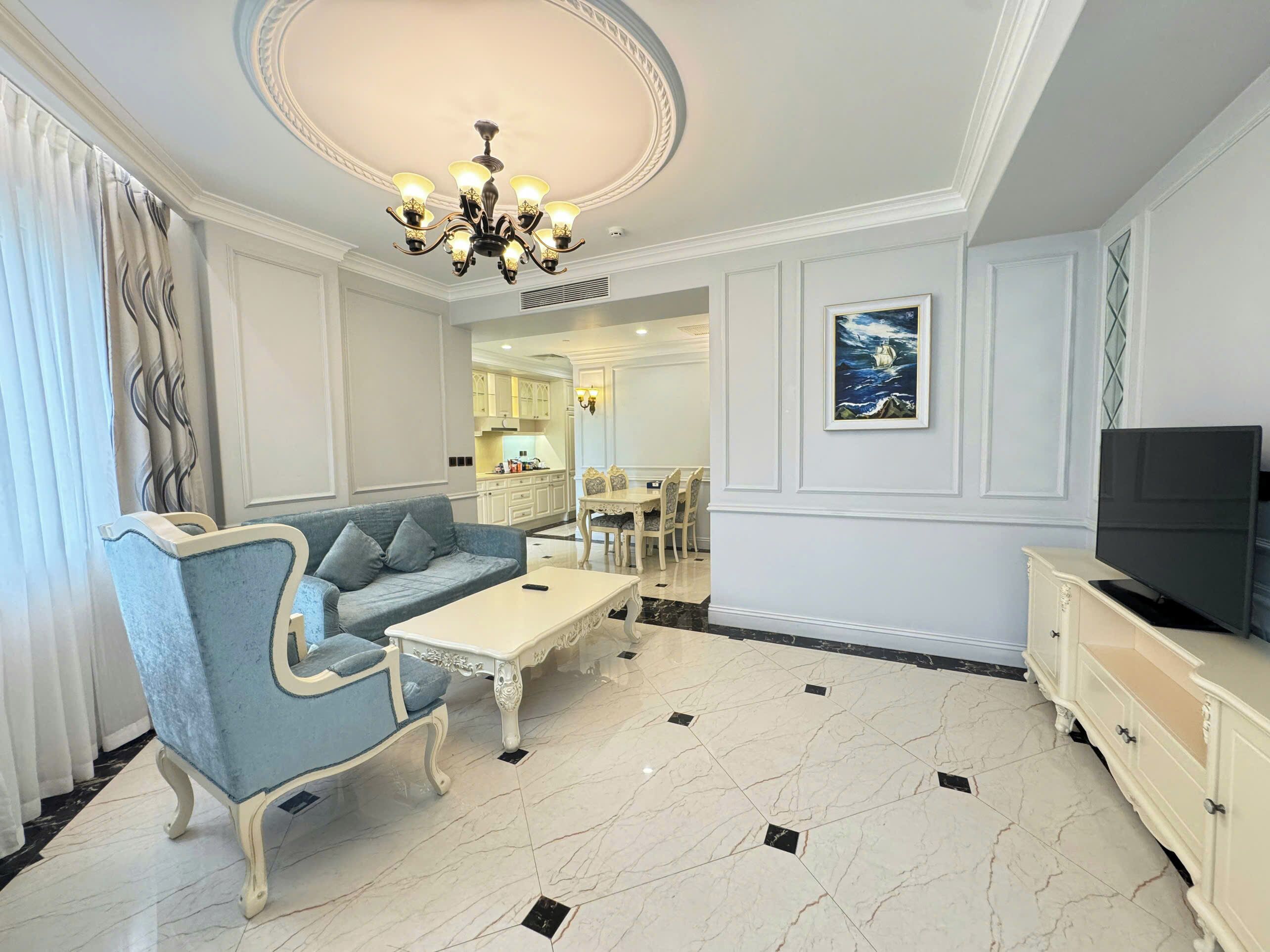 A living room with a blue sofa, a white coffee table, a TV stand, and a chandelier.