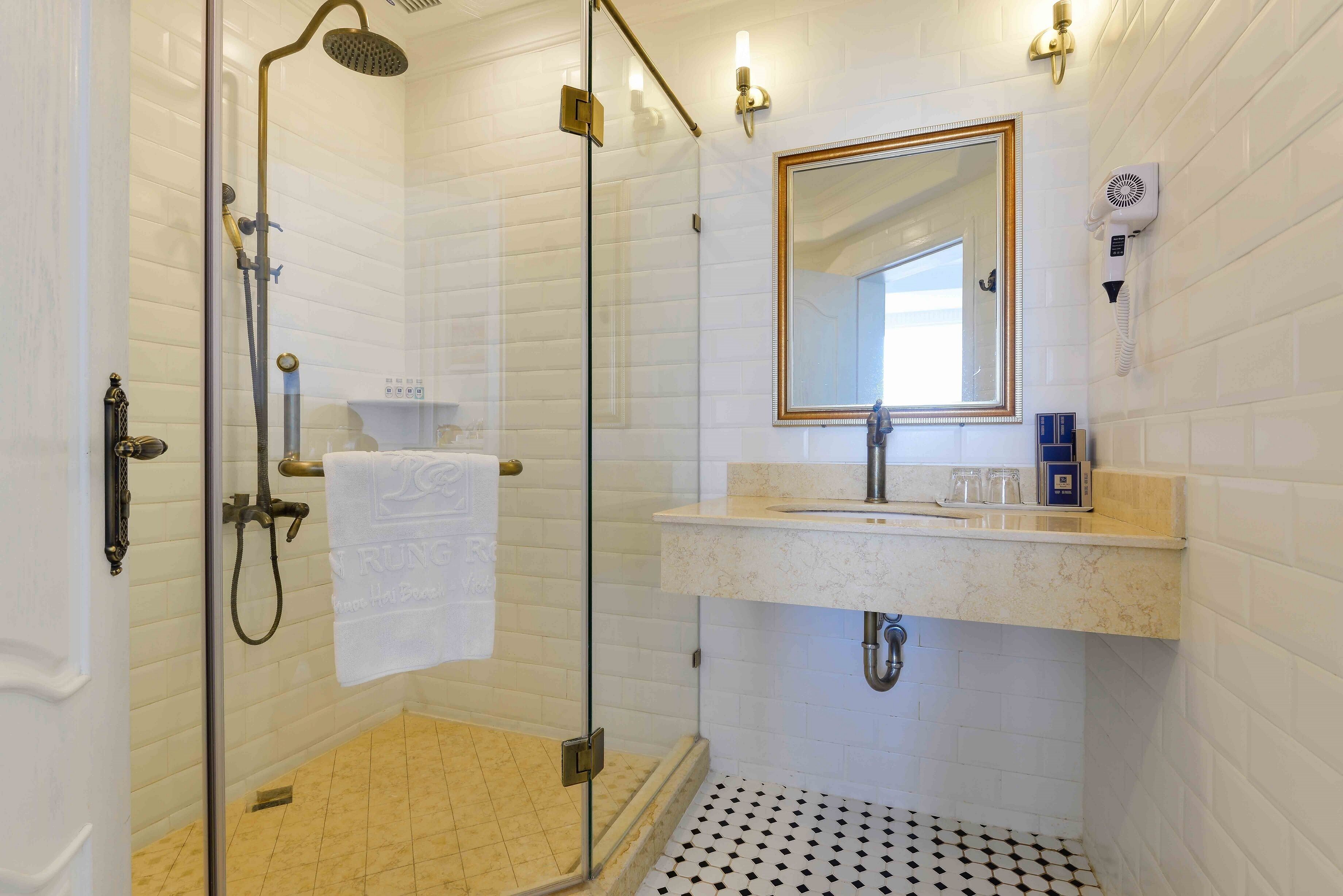A bathroom with a glass-enclosed shower, a sink with a mirror, and a hairdryer mounted on the wall.
