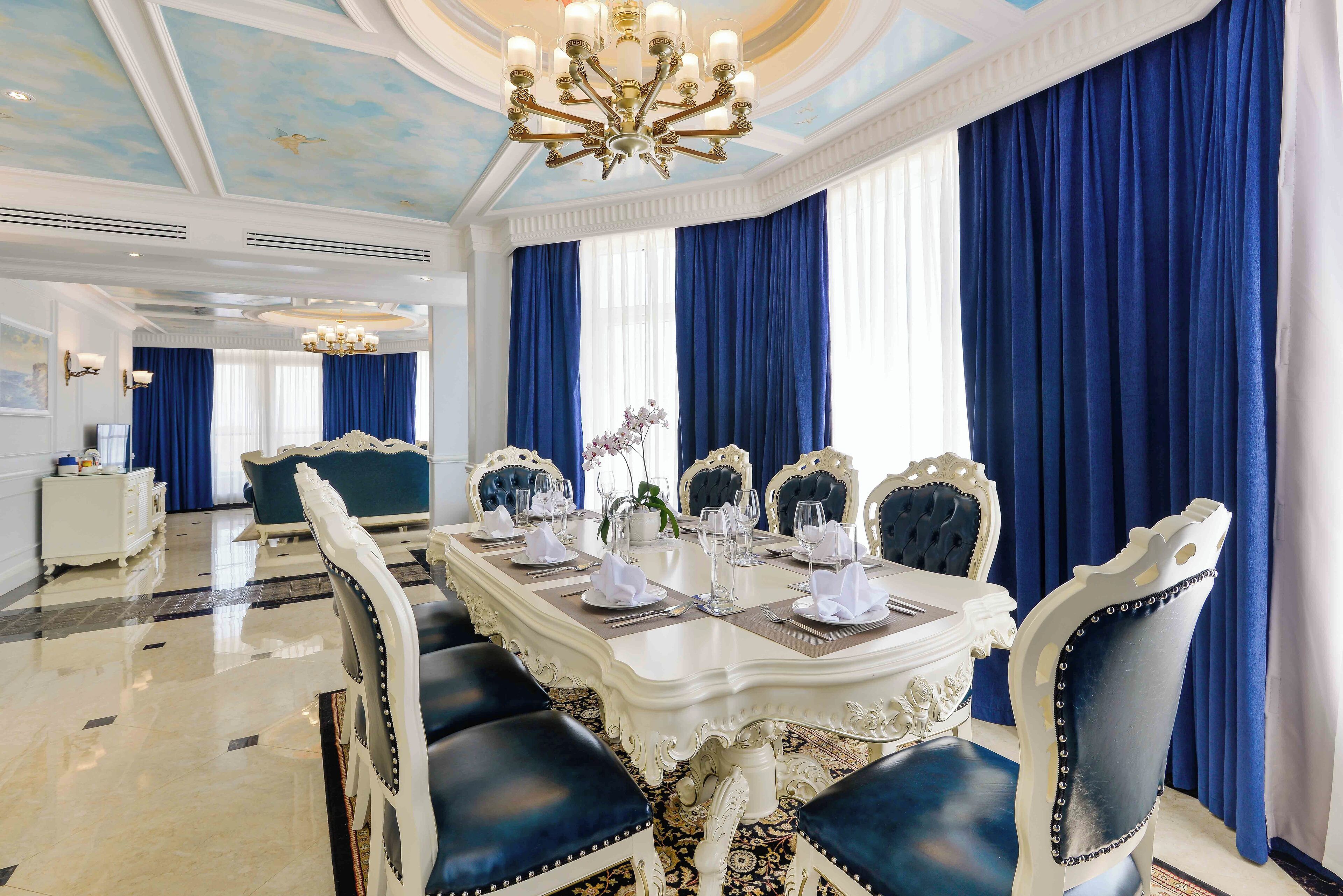 Un comedor formal con una mesa blanca ornamentada dispuesta para seis comensales, sillas tapizadas en azul y un candelabro.