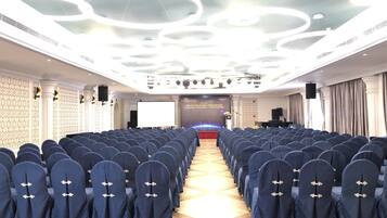 A conference room with rows of blue chairs, a stage with a podium, and a modern ceiling design.