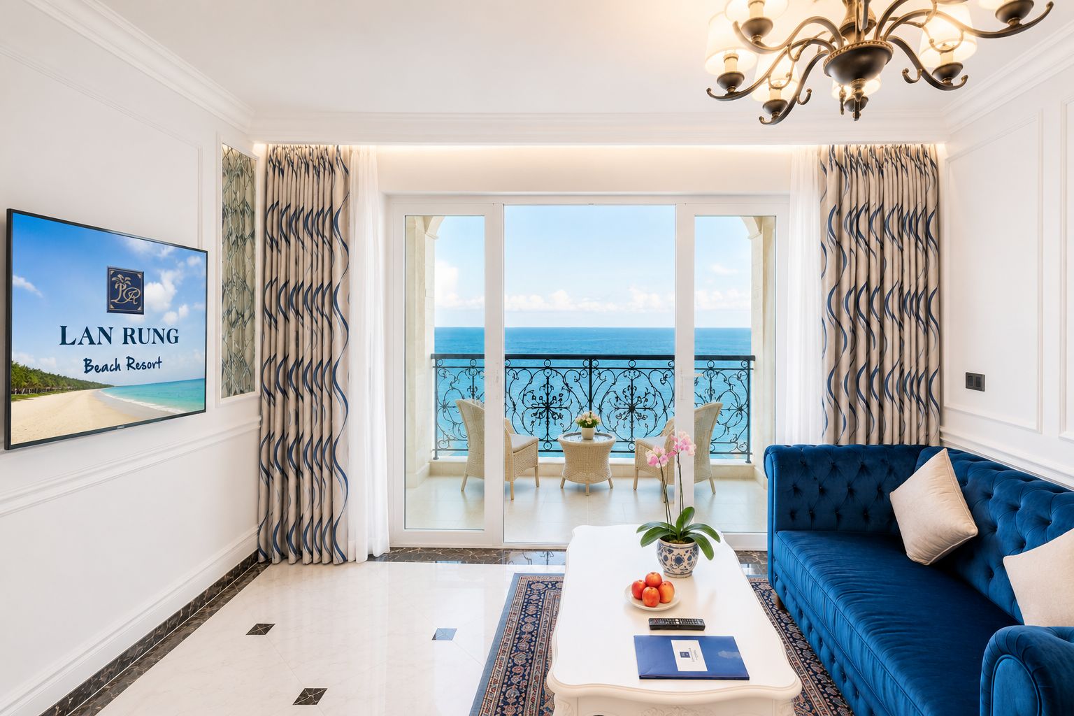 A hotel room with a balcony, a blue sofa, a coffee table with a plant, and a framed picture of a beach.
