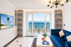 A hotel room with a balcony, a blue sofa, a coffee table with a plant, and a framed picture of a beach. - Lan Rung Beach Resort (Ho Chi Minh City)