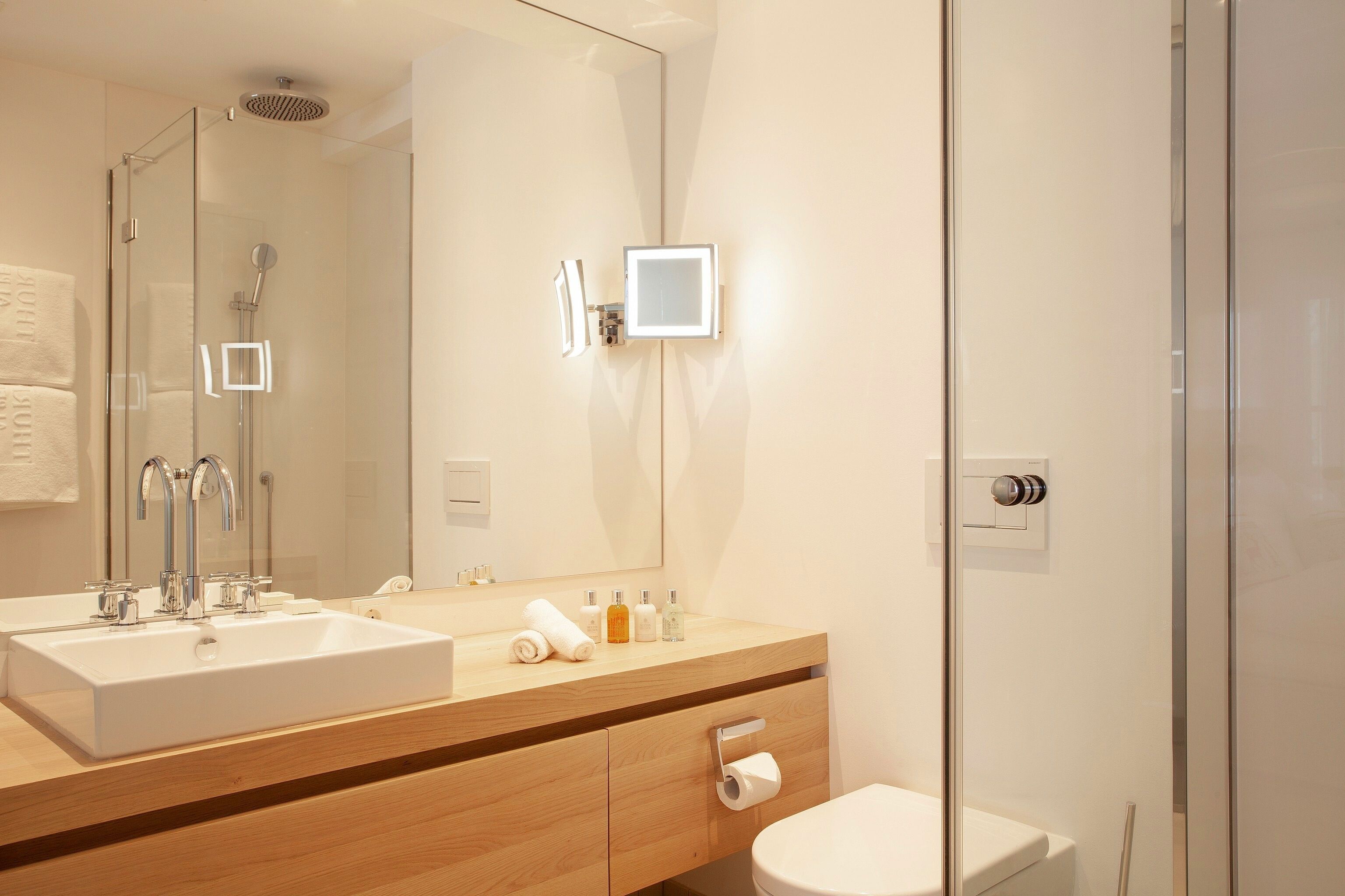 A modern bathroom with a glass shower enclosure, a large mirror, a wooden vanity with a sink, and a toilet.
