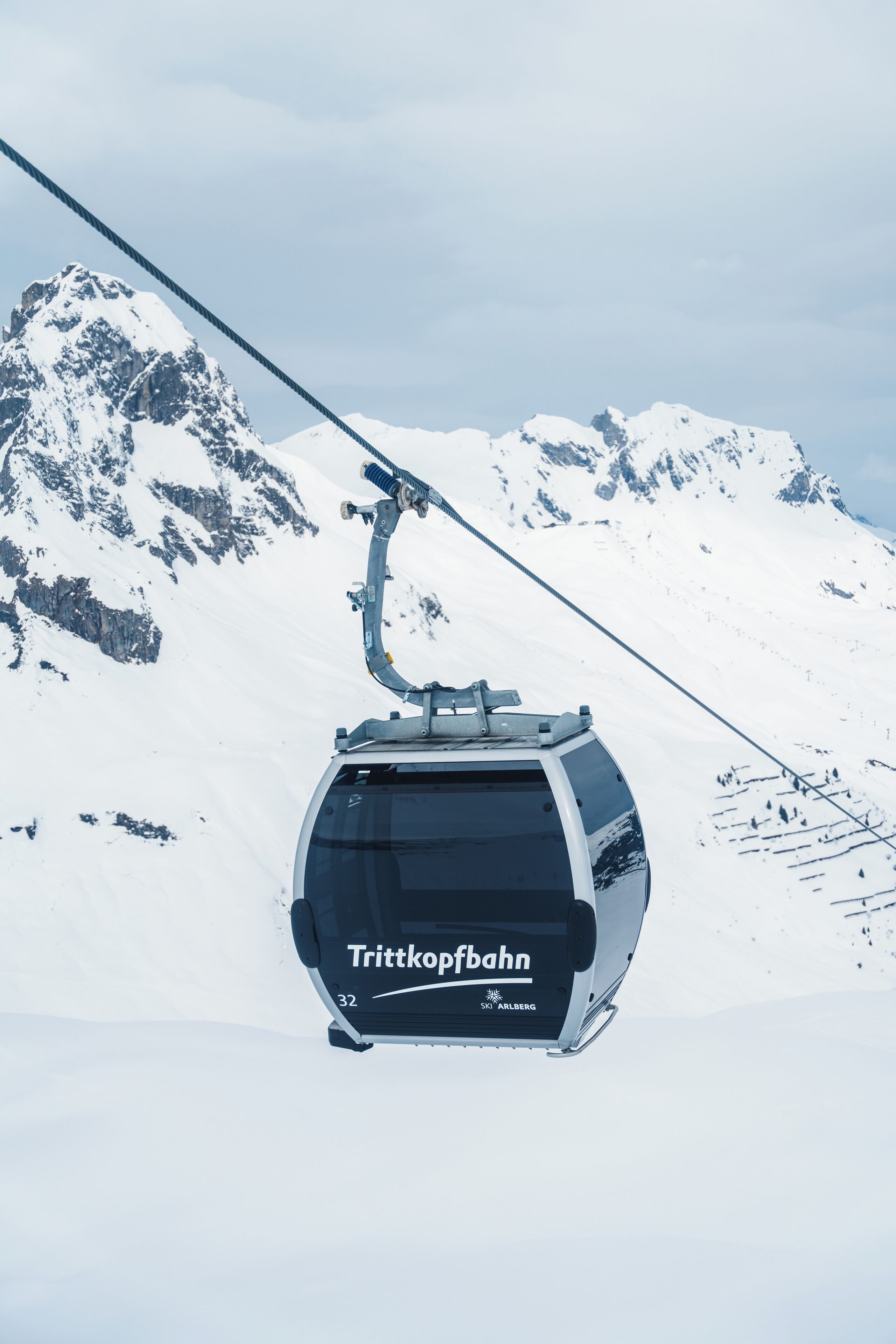 A cable car labeled "Trittkofbahn" at a ski resort with snow-covered mountains in the background.