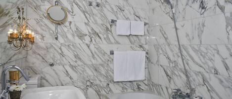 A bathroom with marble walls, a bathtub, a sink, a mirror, and a chandelier.