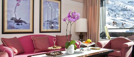 A room with a pink sofa, a dining table with a vase of purple flowers, and framed artwork on the wall.