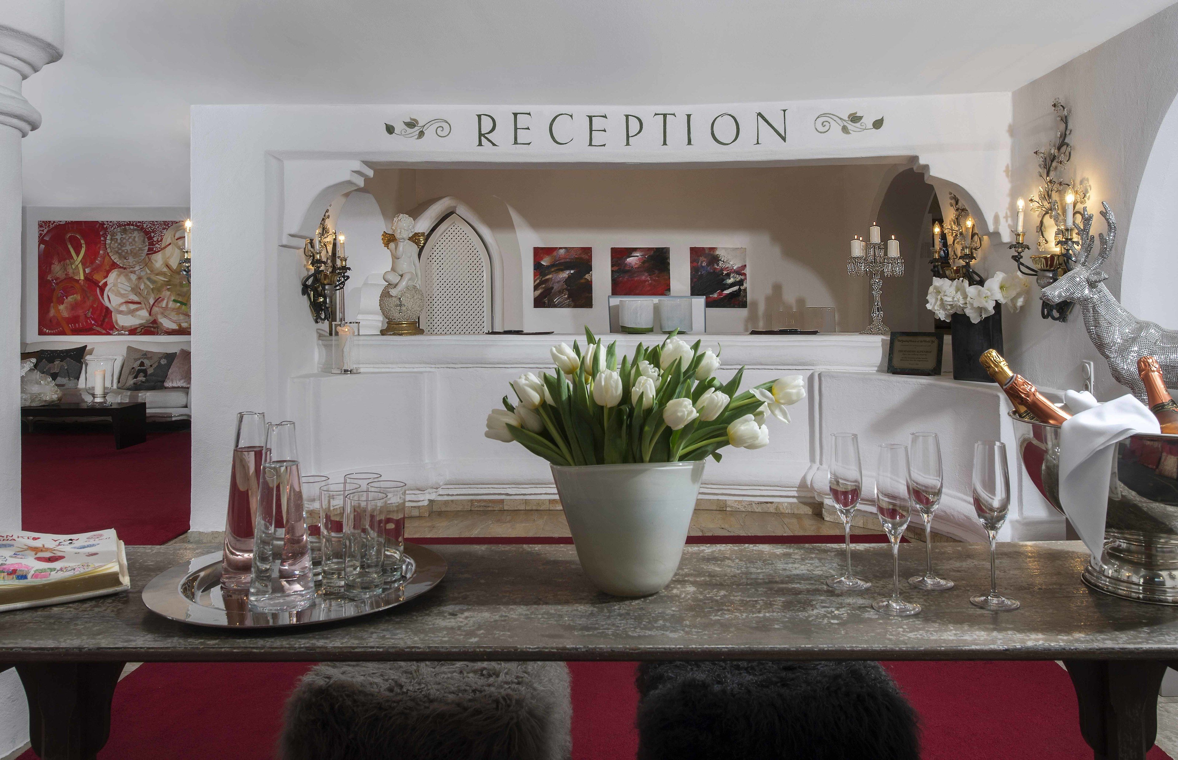 A reception area with a sign, a vase of white flowers, and a tray with glasses and a bottle.