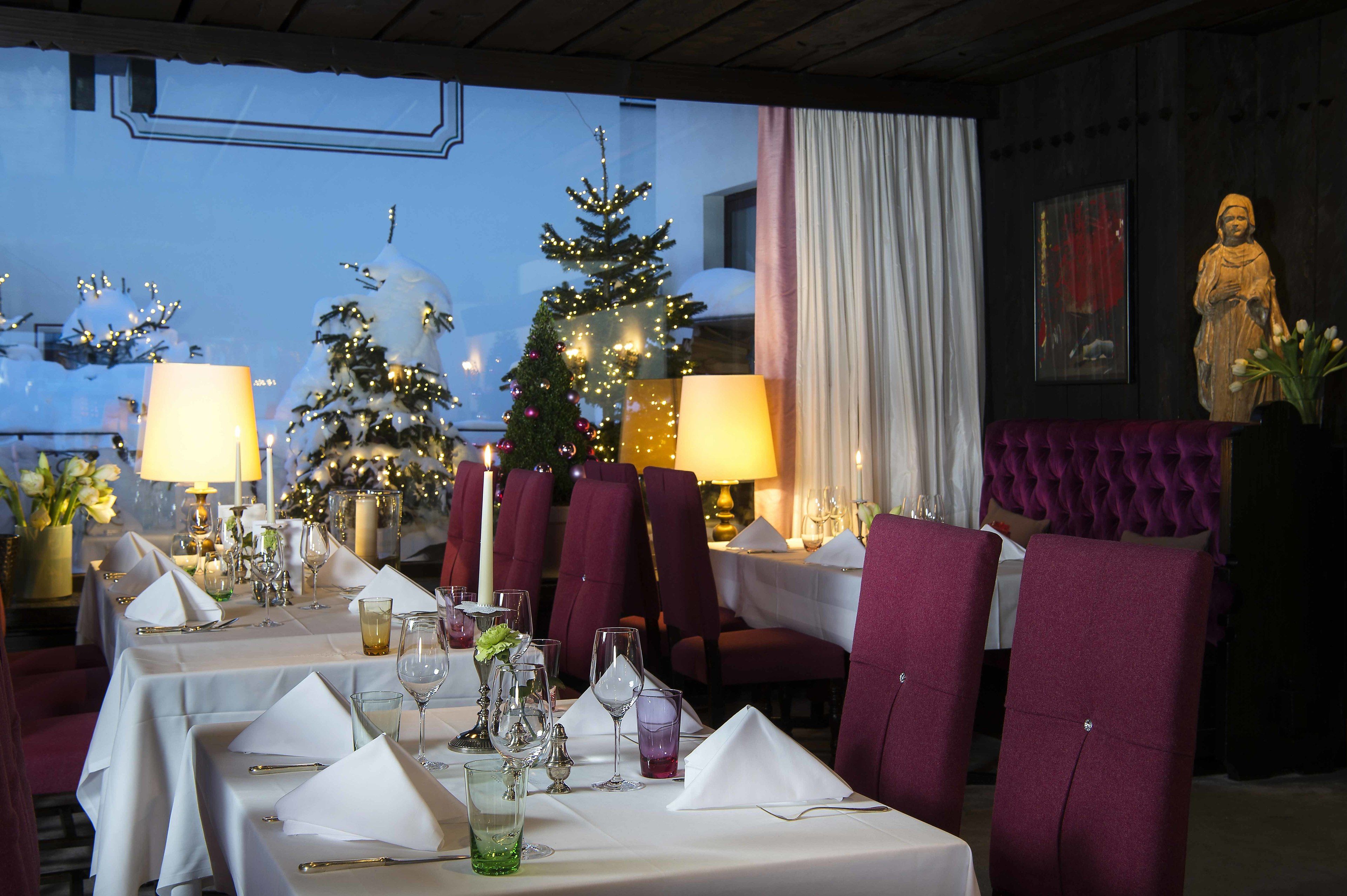 A restaurant with tables set for dining, Christmas trees, and a statue.