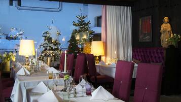 Un restaurant avec des tables dressées pour le dîner, des sapins de Noël et une statue.