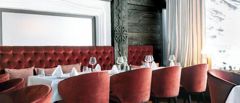 Un restaurante con una cabina tapizada en rojo y sillas rojas, manteles blancos y copas de vino preparadas para una comida.