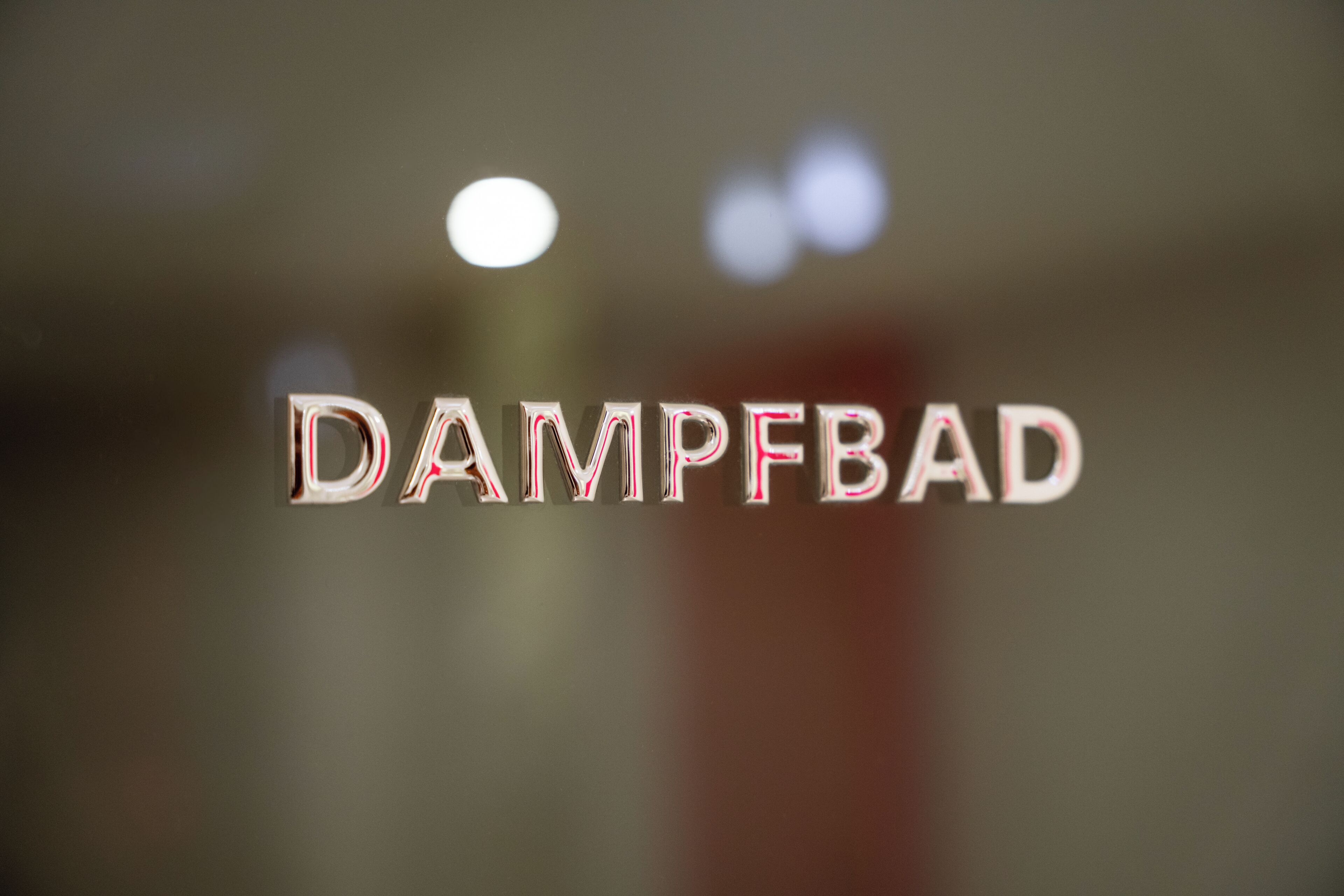 The word "DAMPFBAD" in a metallic font on a blurred background.