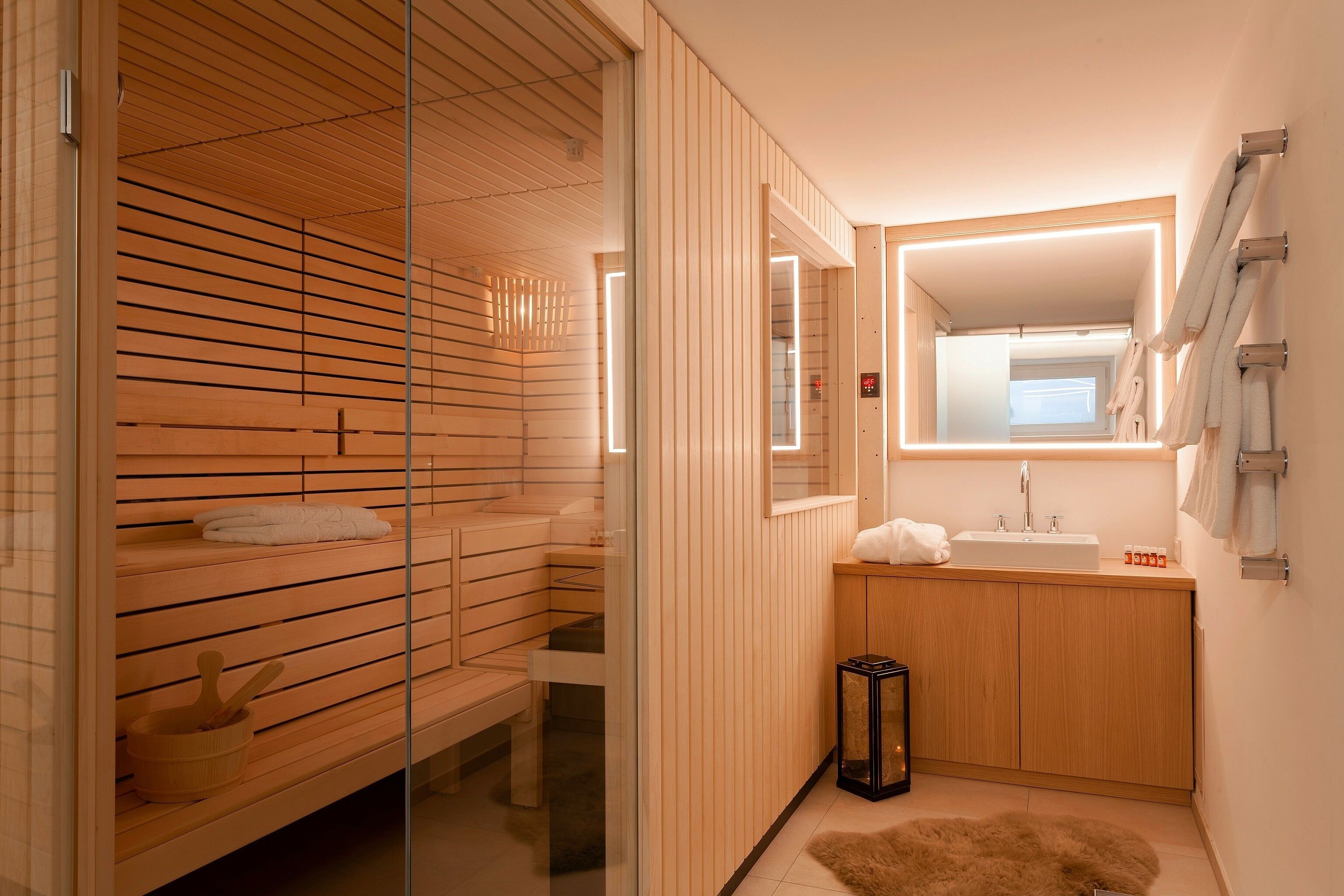A modern bathroom with wooden paneling, a glass shower enclosure, a sink with a mirror, and a small rug.