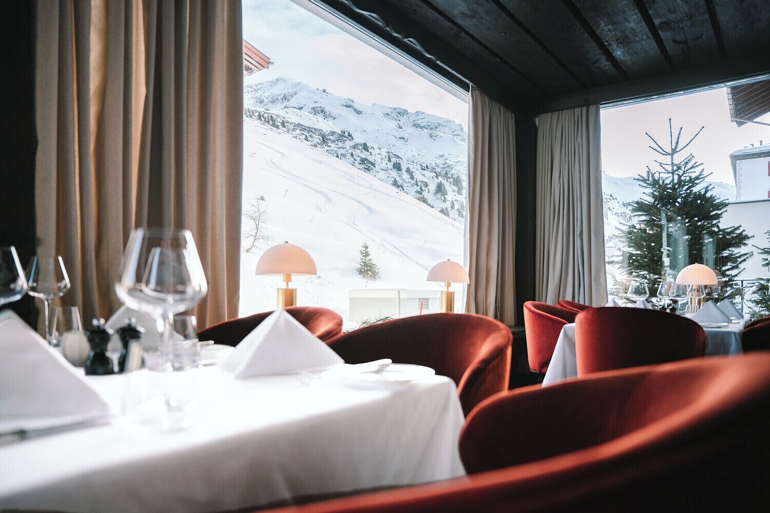 A dining area with a table set for two, a mountain view, and red upholstered chairs.