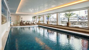 Una amplia piscina interior con sillas de descanso y plantas en macetas a lo largo de las ventanas.