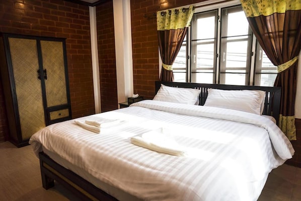 A neatly made bed with white linens and towels, a wooden headboard, and a window with curtains.